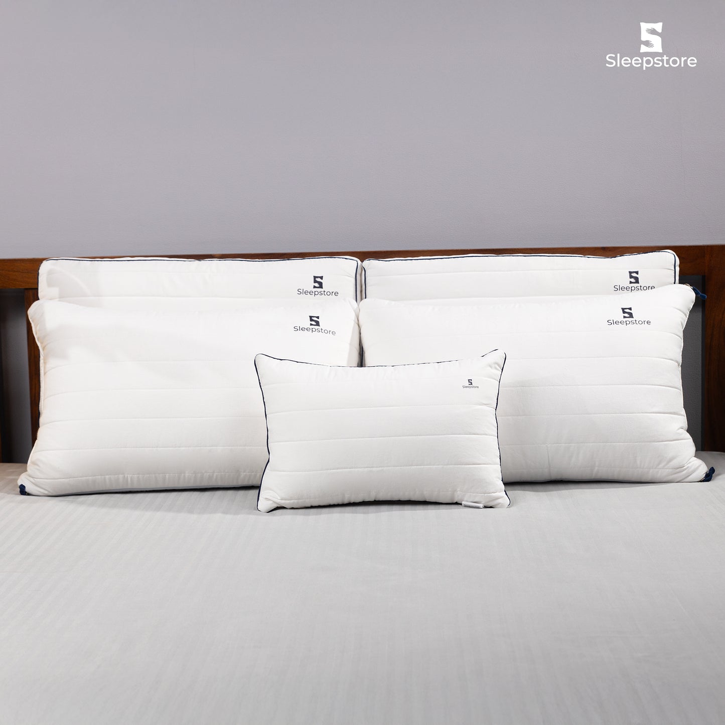 Set of Sleepstore white pillows with black piping, neatly arranged on a bed with a grey sheet.