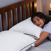 Woman peacefully hugging white Sleepstore pillow with black piping, lying on bed for cozy rest.