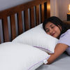 Smiling woman hugging a Sleepstore white pillow while lying on a bed with wooden headboard.