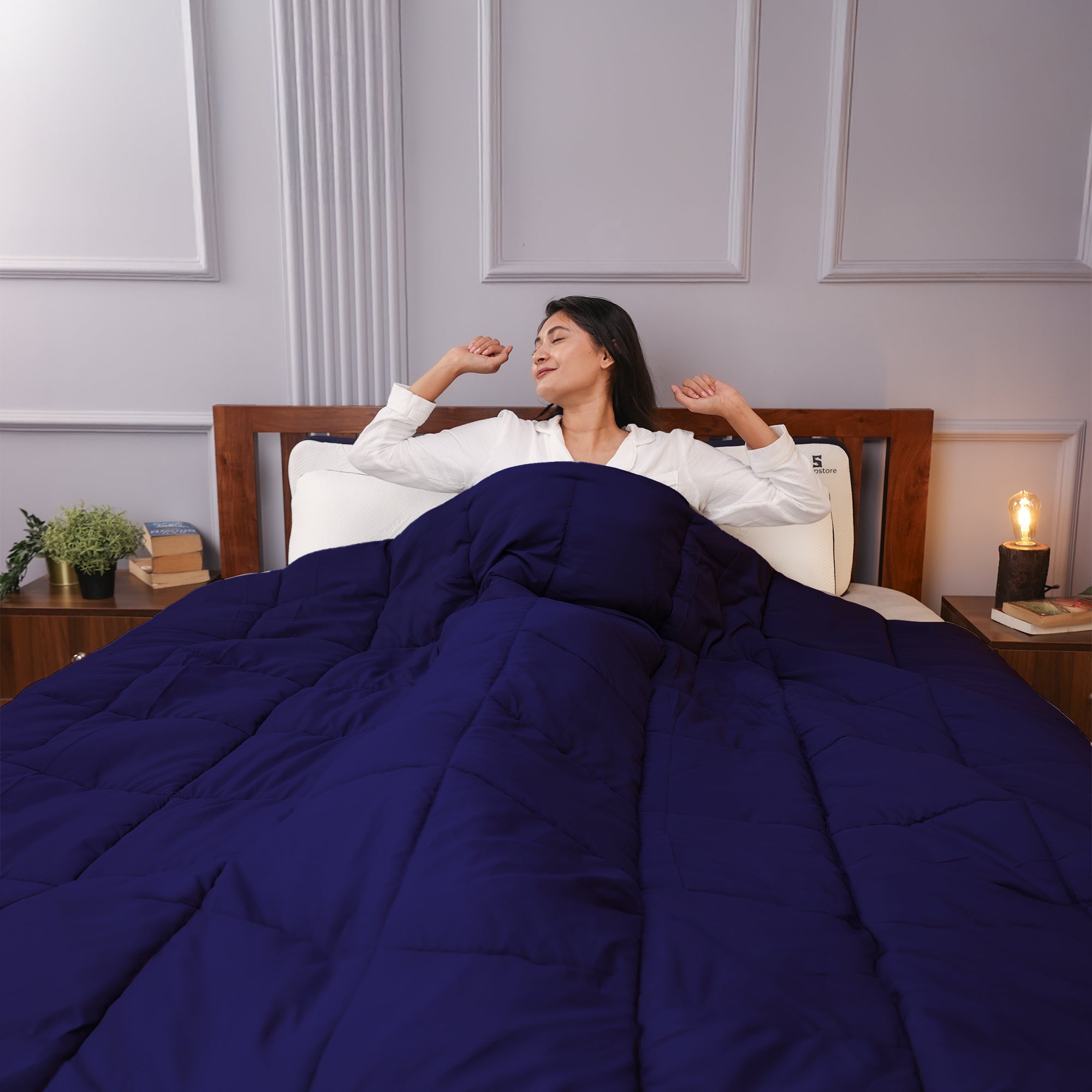 Woman stretching in bed under a navy blue comforter, looking relaxed and refreshed.