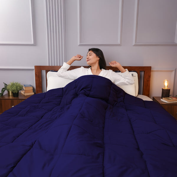 Woman stretching in bed under a navy blue comforter, looking relaxed and refreshed.
