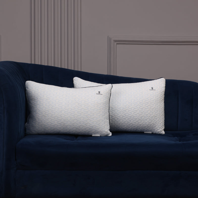 Two white Sleepstore pillows placed on a dark blue velvet sofa against a gray wall.