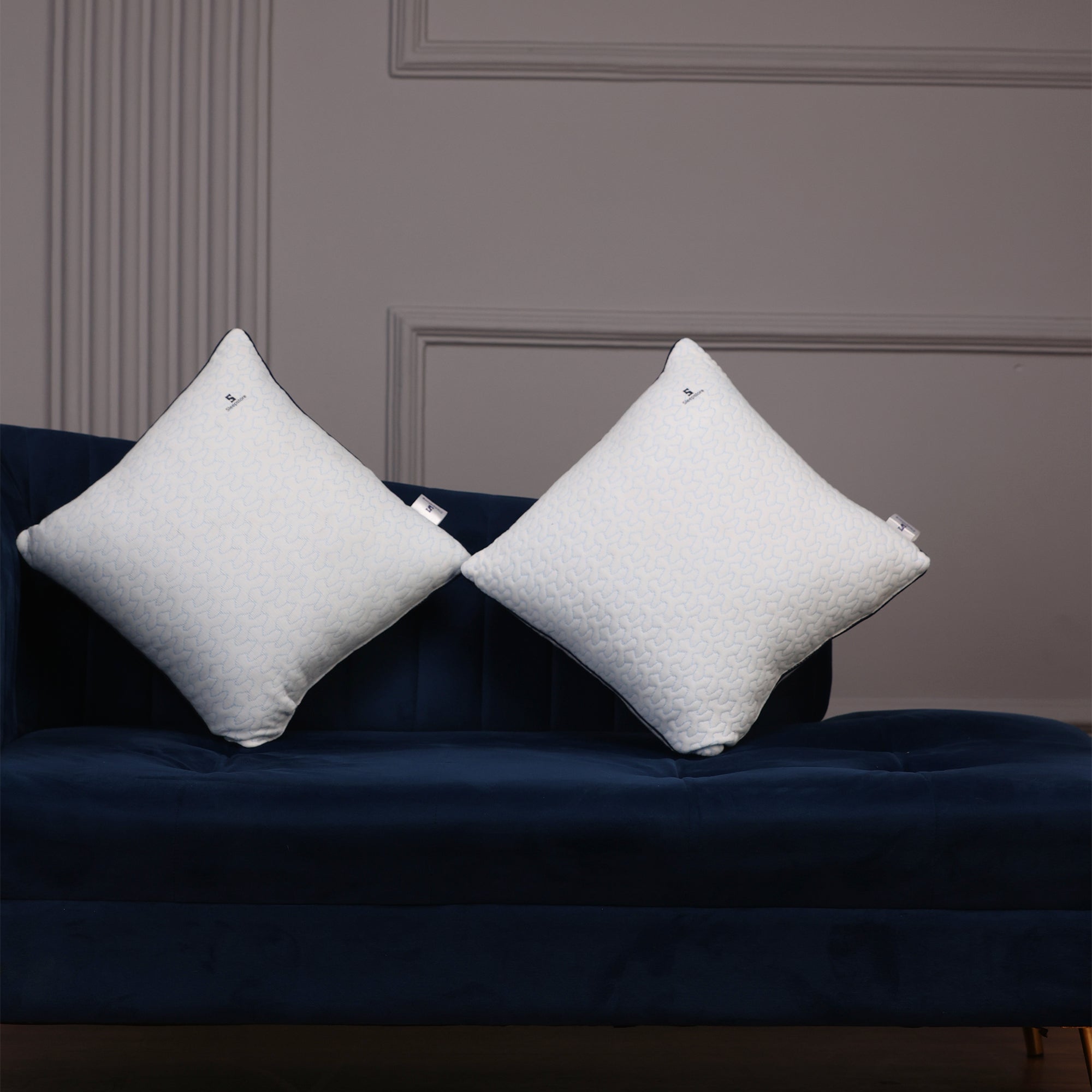 Two white Sleepstore pillows standing upright on a dark blue sofa against a gray wall.