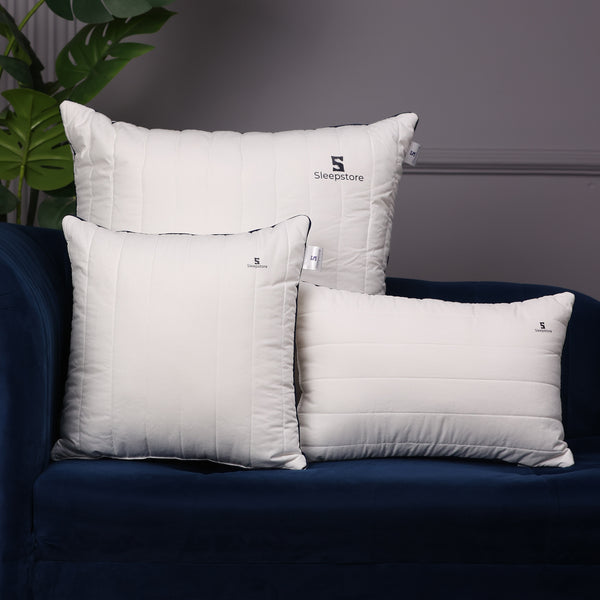 Set of three white Sleepstore pillows in different sizes placed on a dark blue sofa