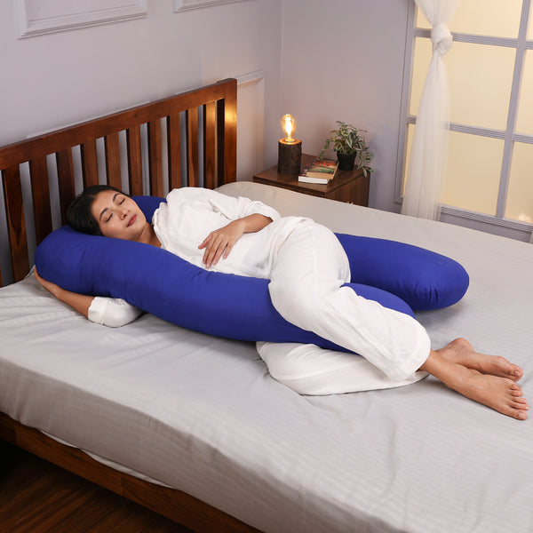 Woman sleeping comfortably on a bed while hugging a large blue body pillow.