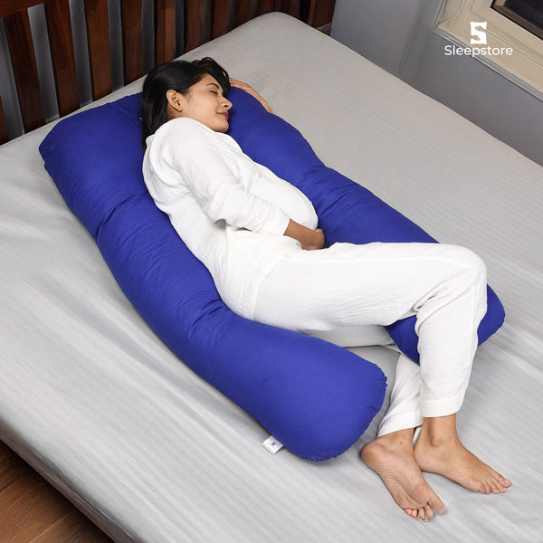Woman lying on bed resting comfortably with a large blue U-shaped body pillow.
