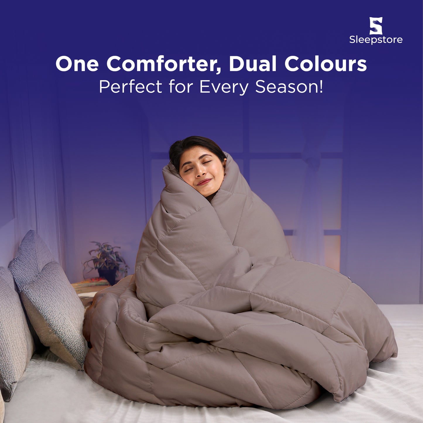 Woman wrapped in a beige dual-color comforter, sitting cozy and smiling on bed.