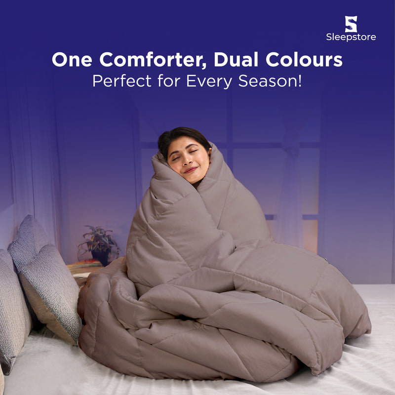 Woman wrapped in a beige dual-color comforter, sitting cozy and smiling on bed.