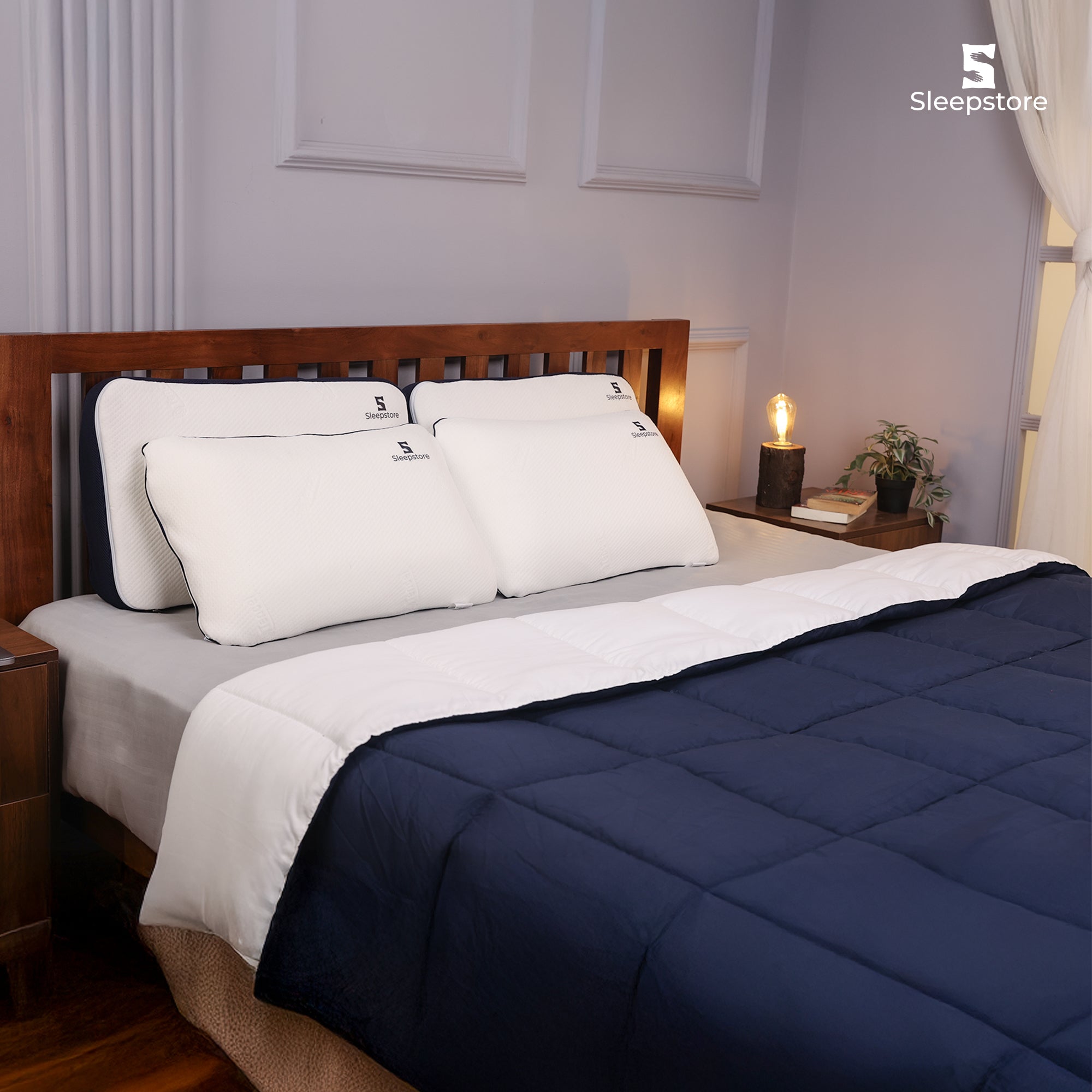 Neatly made bed with navy blue and white comforter, white pillows, and wooden headboard.