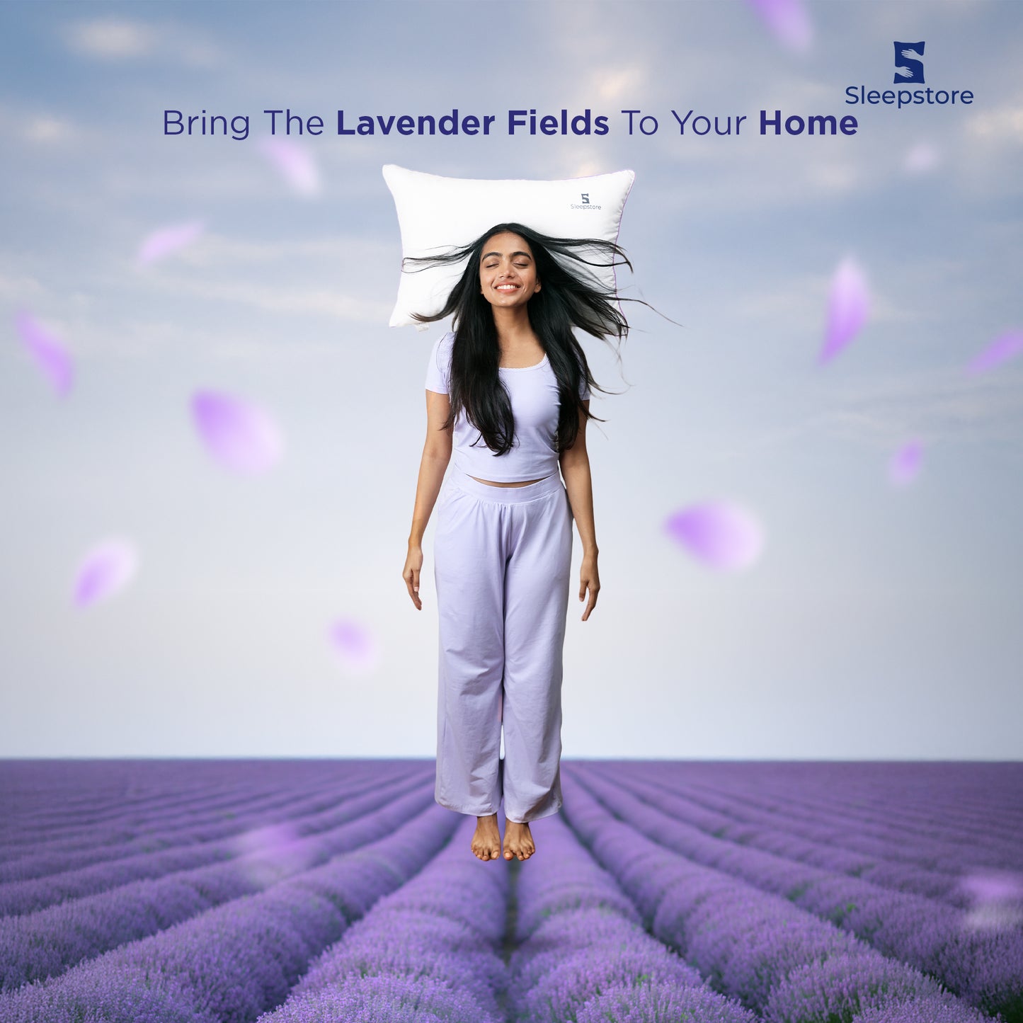 Woman in lavender field smiling with Sleepstore pillow behind head and petals falling.