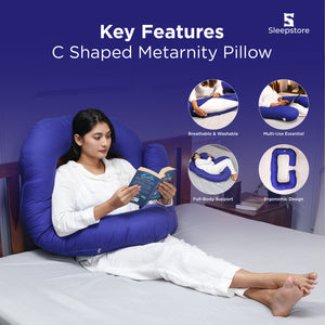 Woman reading a book while using a blue C-shaped maternity pillow on bed.