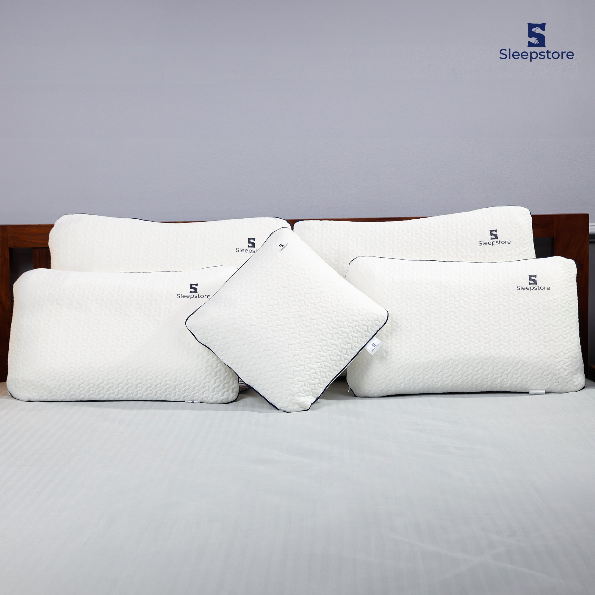 Sleepstore white memory foam pillows in different shapes and sizes arranged on a bed with wooden headboard.